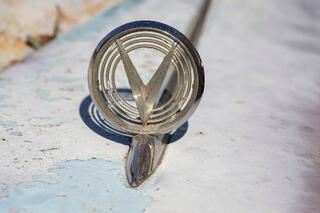 Picture of a 1955 Buick Roadmaster Hood Ornament with V-shaped inset, chrome on fading paint.