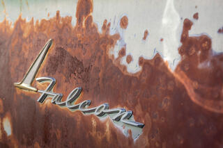 Photo of a 1960s Ford Falcon Emblem with peeling light green paint and exposed rust texture